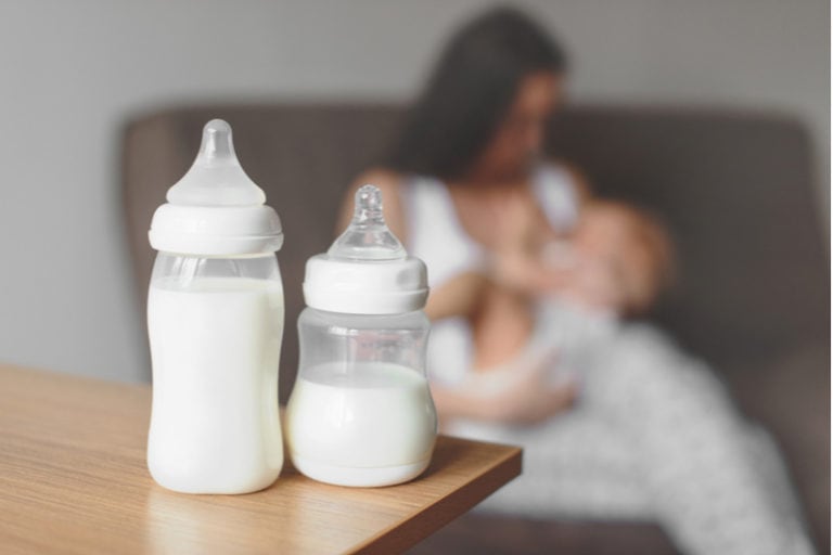 Mutter hält ihr Baby neben zwei mit Milch gefüllten Babyflaschen