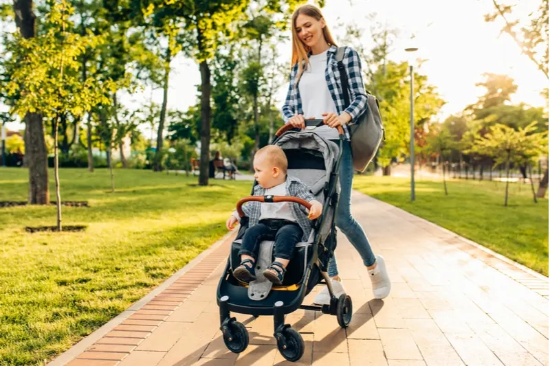 junge Mutter geht mit einem kleinen Kleinkind im Kinderwagen spazieren