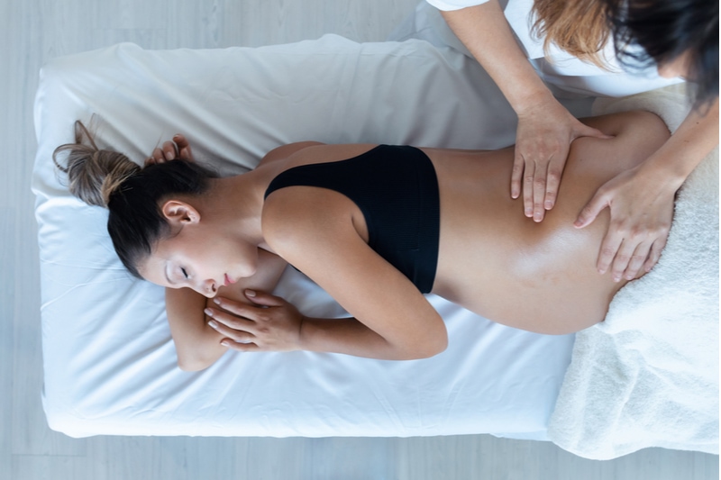 junge Physiotherapeutin massiert Bauch an schwangerer Frau