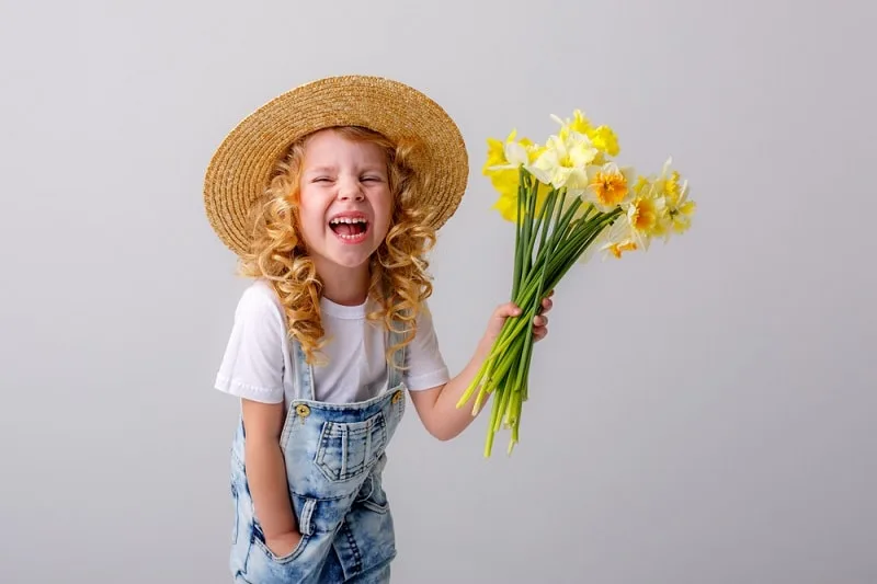 kleines Mädchen mit lockigem blondem Haar lächelt und hält Blumen