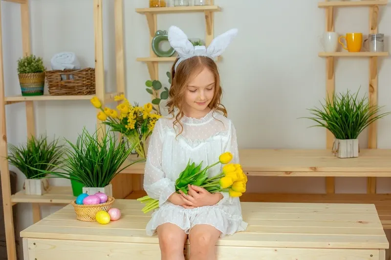 kleines Mädchen mit blonden Haaren hält gelbe Tulpen in der Küche