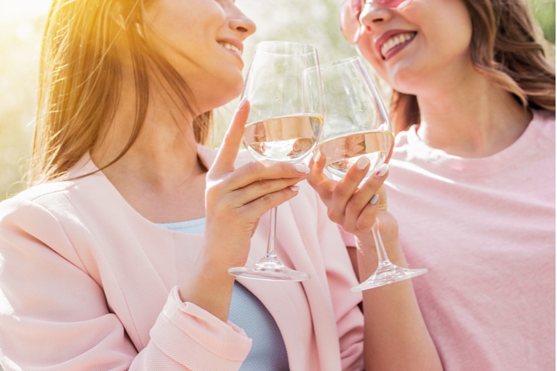 zwei glückliche Frauen jubeln mit Gläsern Weißwein