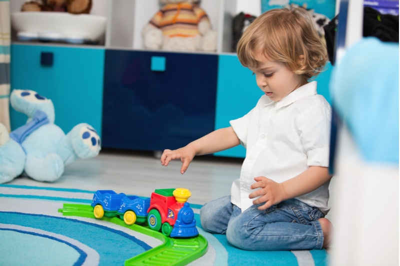 zweijähriges Kind spielt in seinem Zimmer mit einer Spielzeugeisenbahn