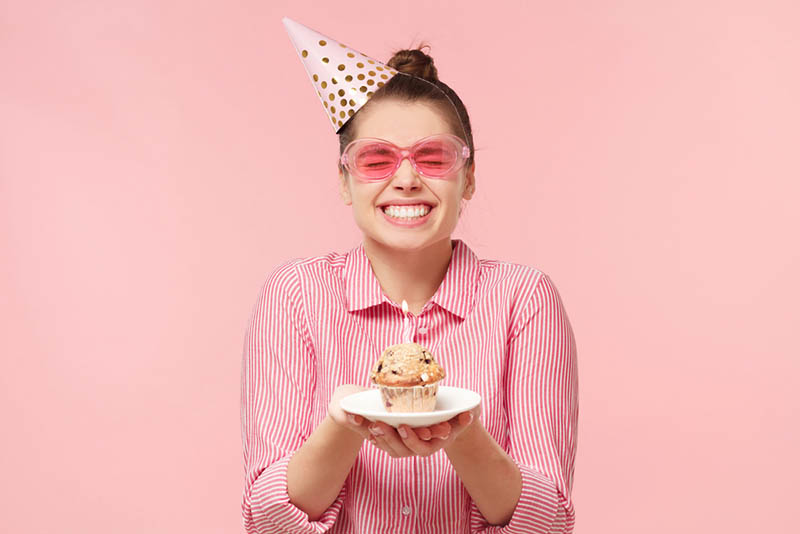 Aufgeregtes lustiges Teenager-Mädchen, das einen Cupcake zum Geburtstag hält
