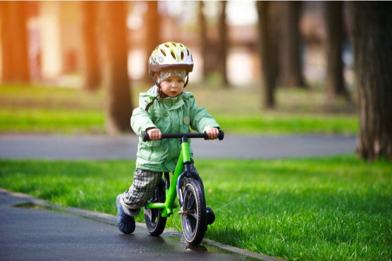kleiner Junge mit Helm und Winterjacke fährt auf einem Laufrad