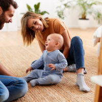 Eltern, die zu Hause auf dem Boden sitzen und mit Baby-Sohn spielen