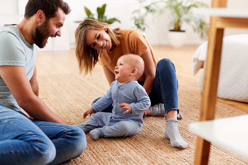 Eltern, die zu Hause auf dem Boden sitzen und mit Baby-Sohn spielen
