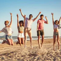 Gruppe aufgeregter Freunde, die Händchen halten, während sie zusammen am Strand springen