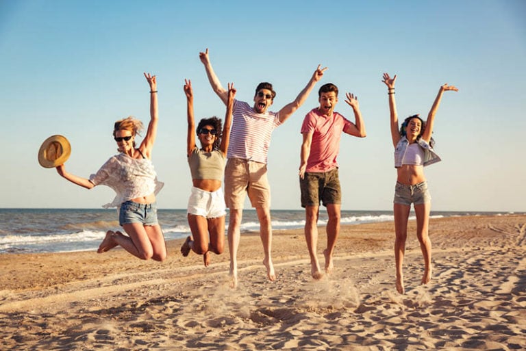 Gruppe aufgeregter Freunde, die Händchen halten, während sie zusammen am Strand springen
