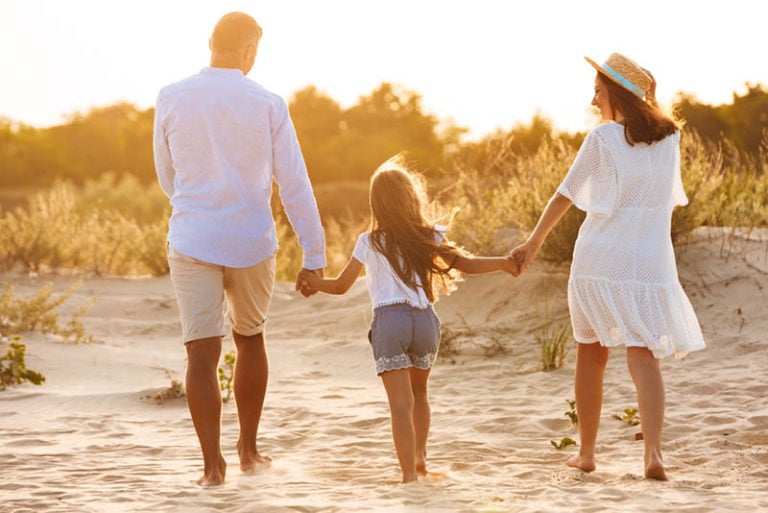 Mama und Papa machen einen Spaziergang mit ihrer Tochter am Strand