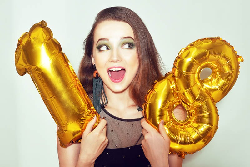 aufgeregtes Mädchen feiert Geburtstag mit goldenen Zahl Luftballons