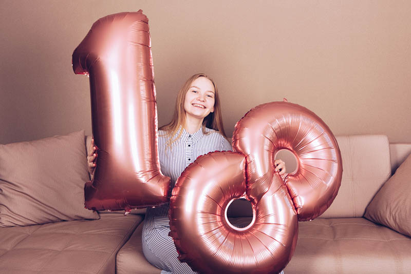 glückliches Mädchen, das seinen 18. Geburtstag mit großen Ballonzahlen feiert