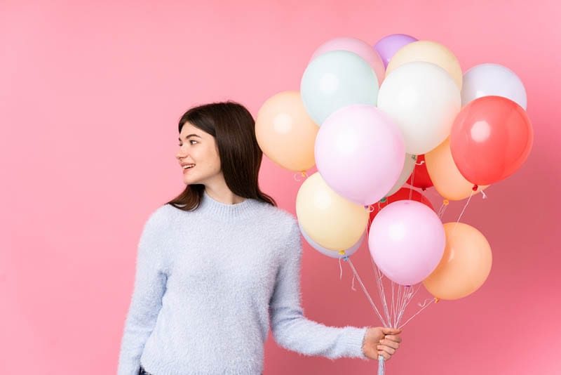 junges Mädchen hält einen Haufen Luftballons