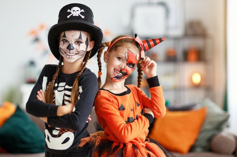 Zwei Kinder in Anzügen und mit Kürbissen zu Hause an Halloween