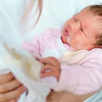 Mutter hält ihr neugeborenes Baby, das Milch spuckt