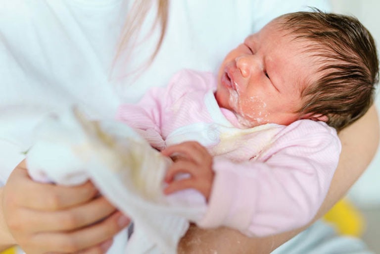 Mutter hält ihr neugeborenes Baby, das Milch spuckt