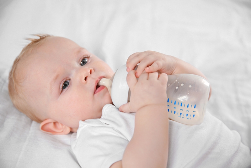 Baby trinkt Milch aus der Flasche, während es auf dem Bett liegt
