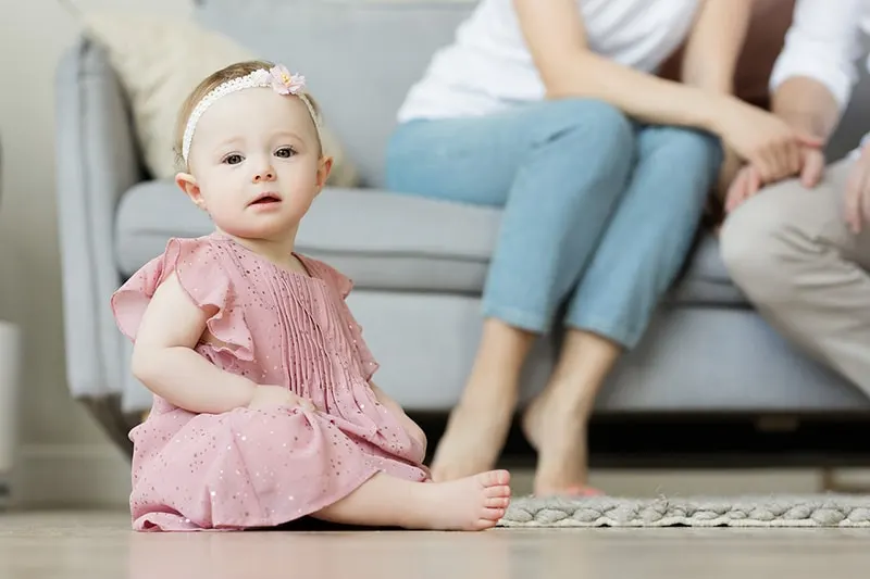 Baby Mädchen sitzt auf dem Boden vor den Eltern sitzen auf der Couch