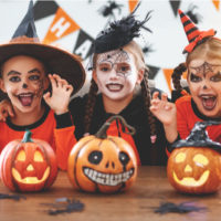 drei Kinder in gruseligen Halloween-Kostümen posieren vor Kürbissen