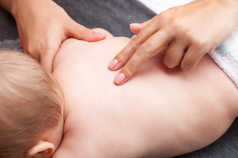 Die Wirbelsäule des Babys wird von einem osteopathischen Therapeuten manipuliert, während es auf dem Bett liegt