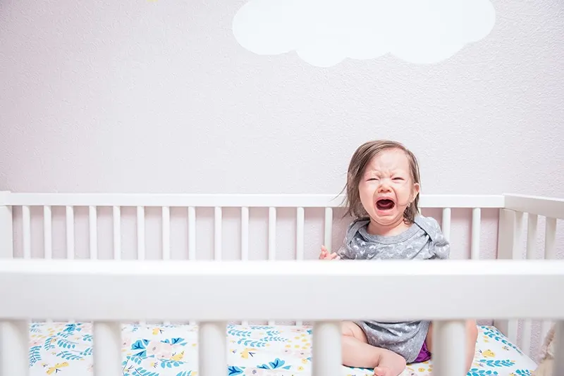 Ein Baby wacht weinend und schreiend in seinem Bettchen auf