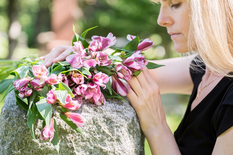 Eine trauernde Frau am Grabstein auf dem Friedhof, die die Blumen berührt