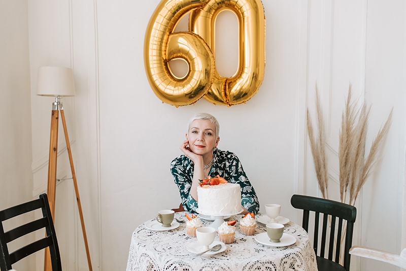 Frau feiert 60. Geburtstag am Tisch sitzend mit Kuchen drauf