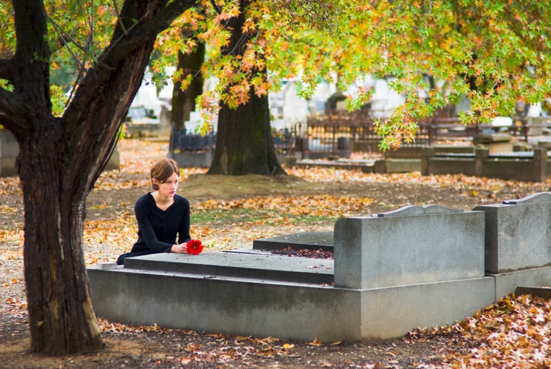 Frau legt Blumen auf Grab auf dem Friedhof