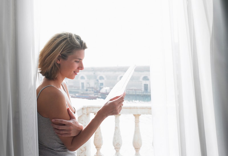 Frau liest einen Brief, während sie auf dem Balkon steht