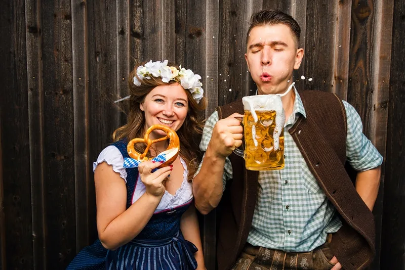 Frau mit Brezel und Mann mit Bier, während sie in der Nähe der Holzwand steht