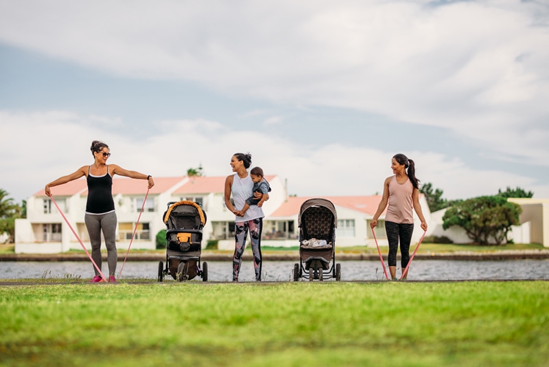 Frauen trainieren im Park und bringen ihre Kinder in Kinderwagen