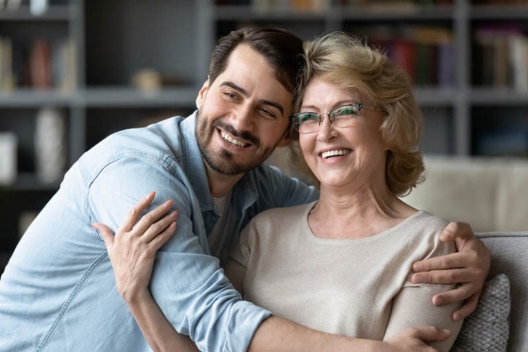lächelnder junger Mann, der seine Mutter umarmt