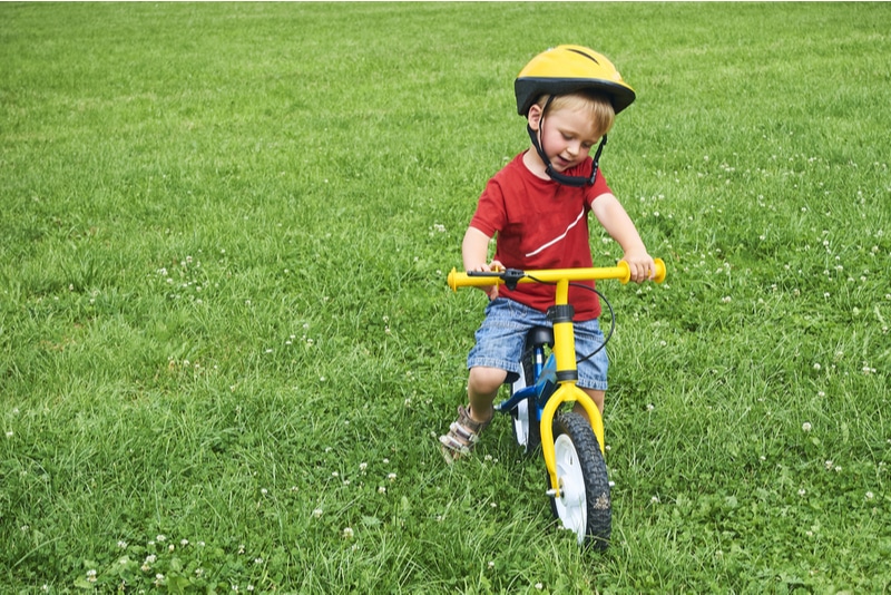 Glückliches Kleinkind Kind Junge, das Fahrrad ohne Pedale fährt
