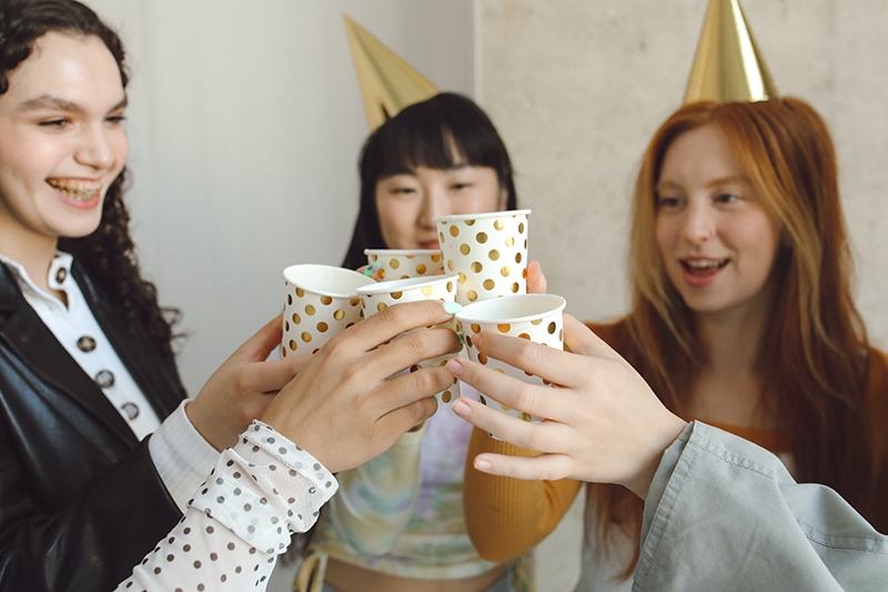 Gruppe fröhlicher Freundinnen, die auf der Geburtstagsfeier mit Getränken anstoßen