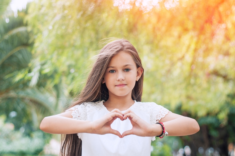 Hübsches kleines Mädchen, das ein Herzsymbol im Park zeigt
