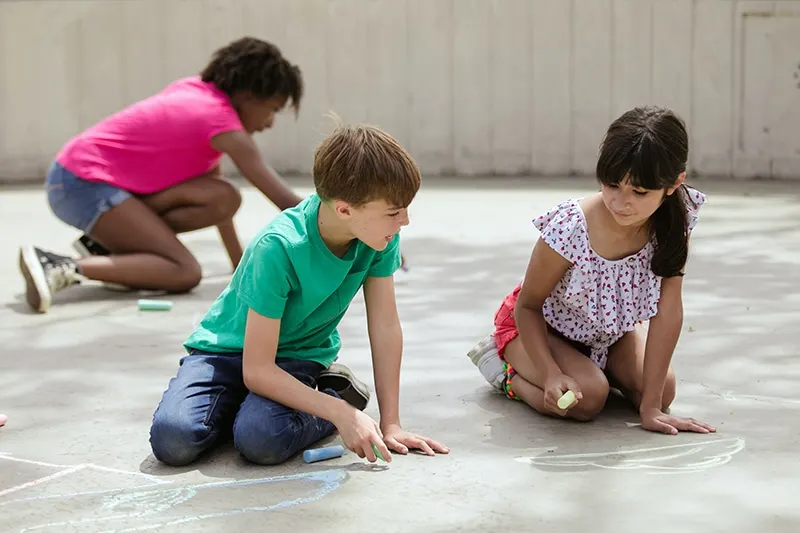 Junge und Mädchen reden beim Zeichnen mit Kreide auf Beton