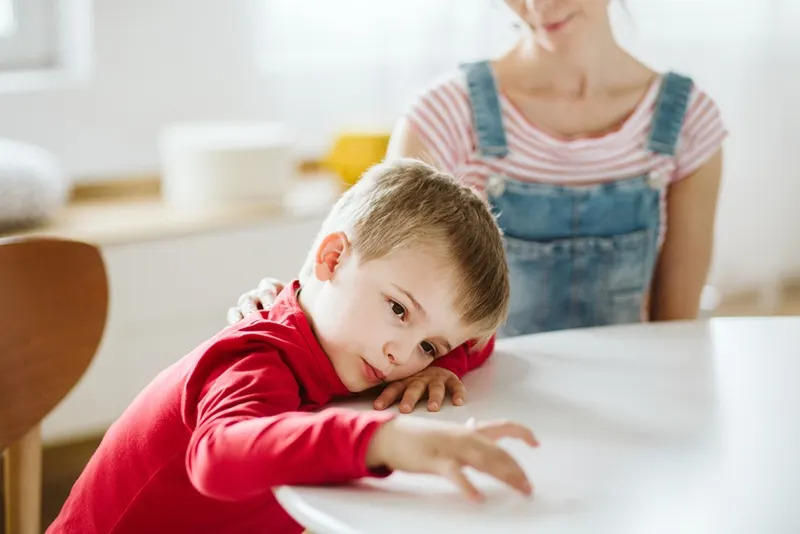 Kind mit ADHS achtet nicht auf seine Mutter und lehnt den Kopf auf den Tisch