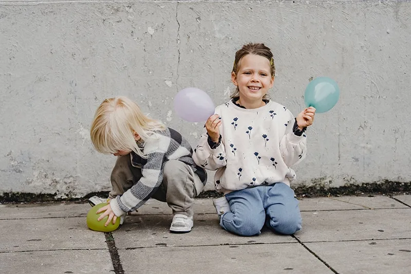 Kinder, die Luftballons halten, während sie auf dem Betonboden sitzen
