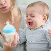 Mutter versucht weinendes Baby mit einer Flasche Milch zu füttern