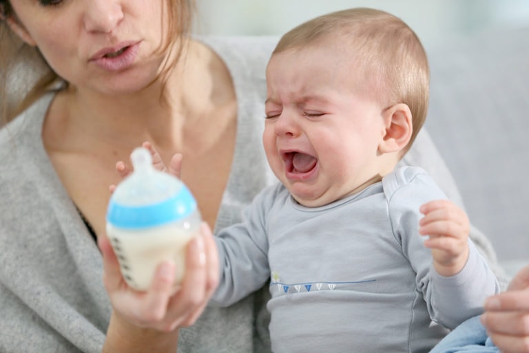 Mutter versucht weinendes Baby mit einer Flasche Milch zu füttern