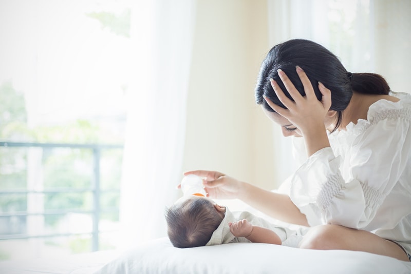 Mutter füttert neugeborenes Baby mit Formel auf dem Bett