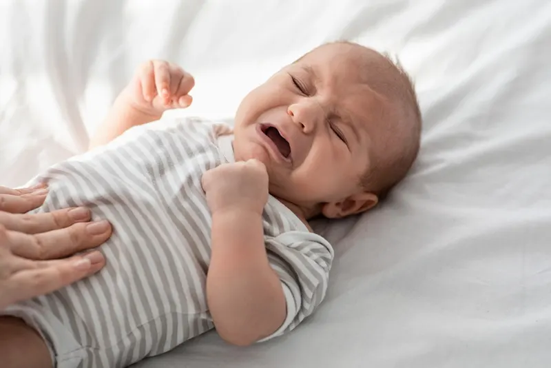 Mutter massiert ihrem weinenden Baby, das auf dem Bett liegt, den Bauch