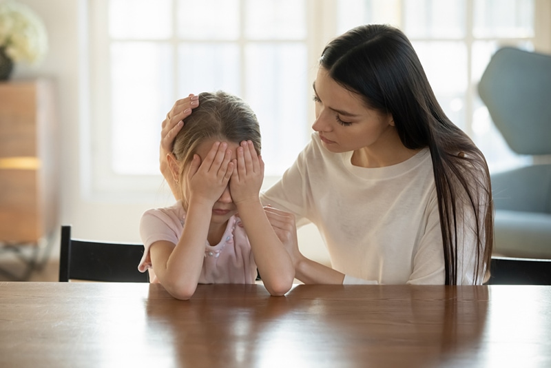 Mutter tröstet weinende Tochter, während sie zu Hause am Tisch sitzt