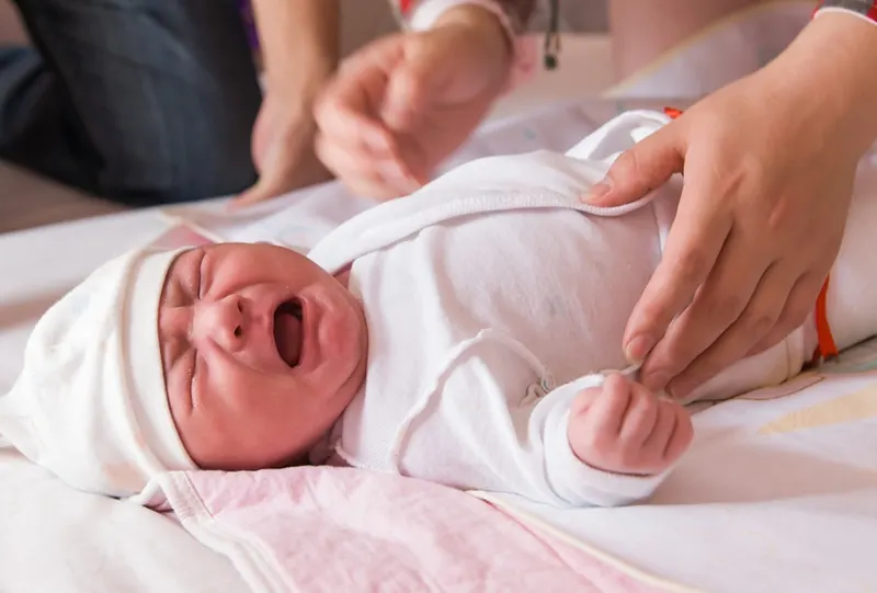 Neugeborenes Baby weint auf dem Bett, während Mutter versucht, sie in die Hände zu nehmen