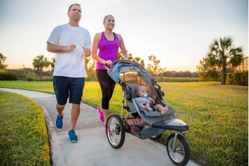 Paare, die zusammen im Park trainieren und joggen und ihr Baby in einem Kinderwagen schieben