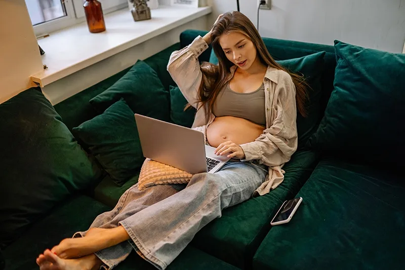 Schwangere Frau entspannt sich und benutzt Laptop auf der Couch