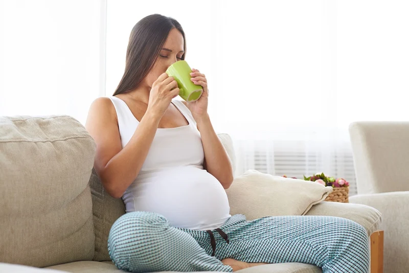 Schwangere trinkt Tee, während sie auf der Couch sitzt