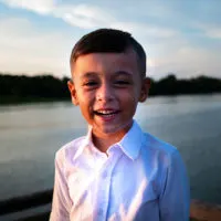 lächelnder kleiner Junge, der in der Nähe des Sees steht