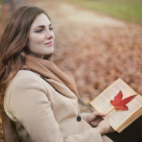 positive Frau, die ein Buch hält, während sie auf der Bank sitzt