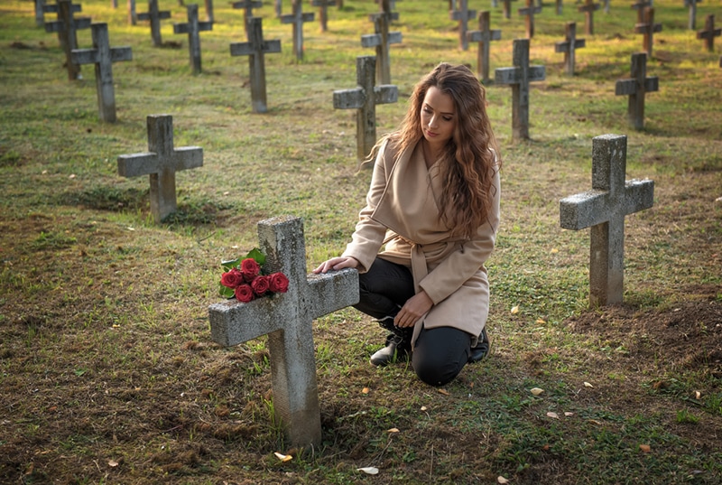 Traurige Frau auf dem Friedhof, die das Grab ihrer Freundin berührt